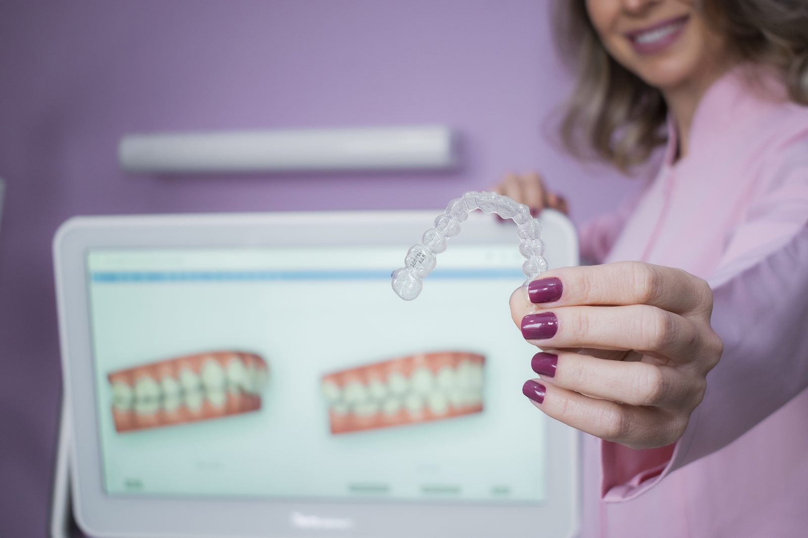 Dra. Gabriela Cavalheiro segurando um alinhador Invisalign, com simulação digital do sorriso ao fundo